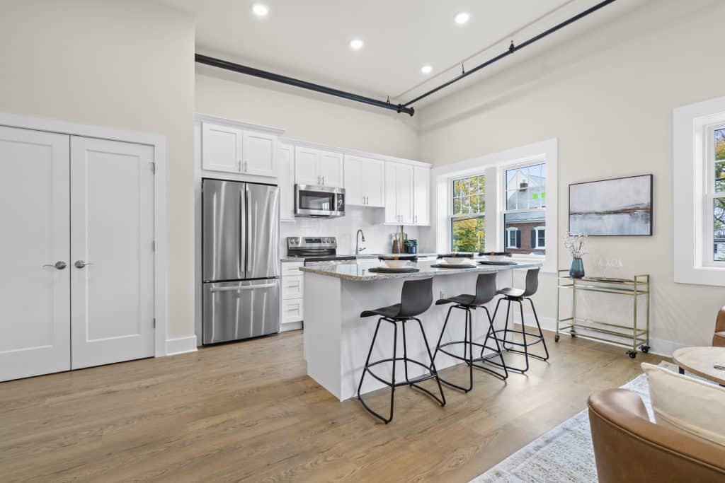 Modern kitchen at Lofts on Broad with white cabinets, granite island with 3 black stools, stainless appliances, large windows.