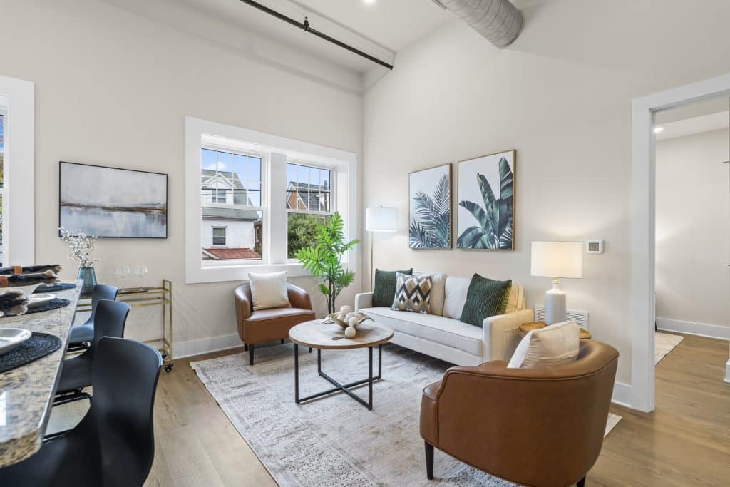 Bright living room at Lofts on Broad in Souderton with a white sofa, two brown leather chairs and a round wood coffee table.