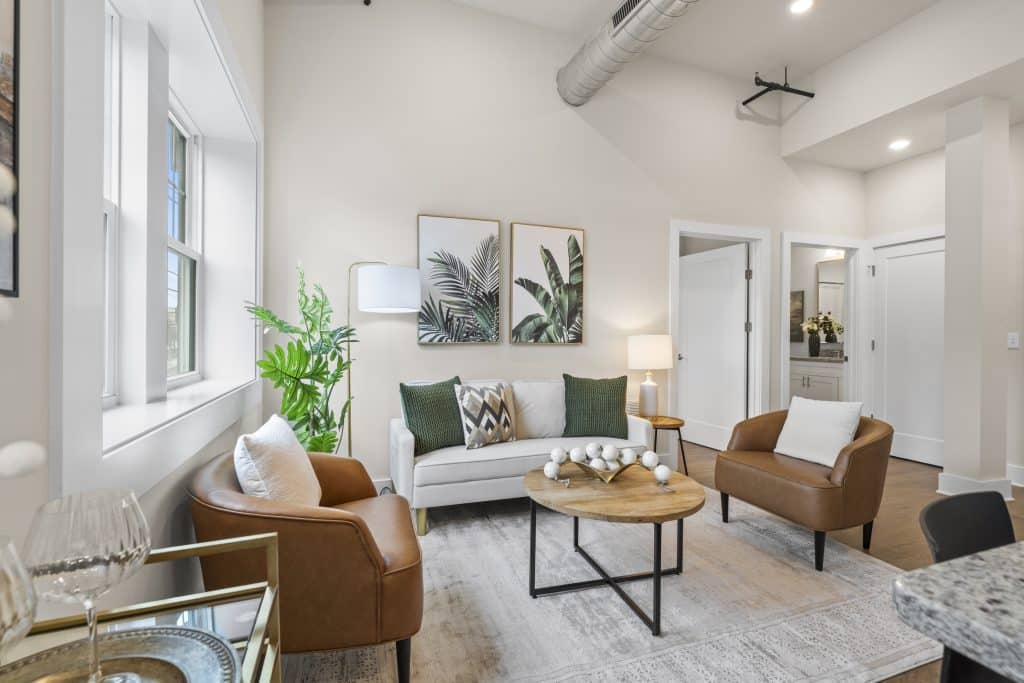 Lofts on Broad living room with vaulted ceiling, exposed duct, sofa, leather chairs, wood coffee table and botanical art.