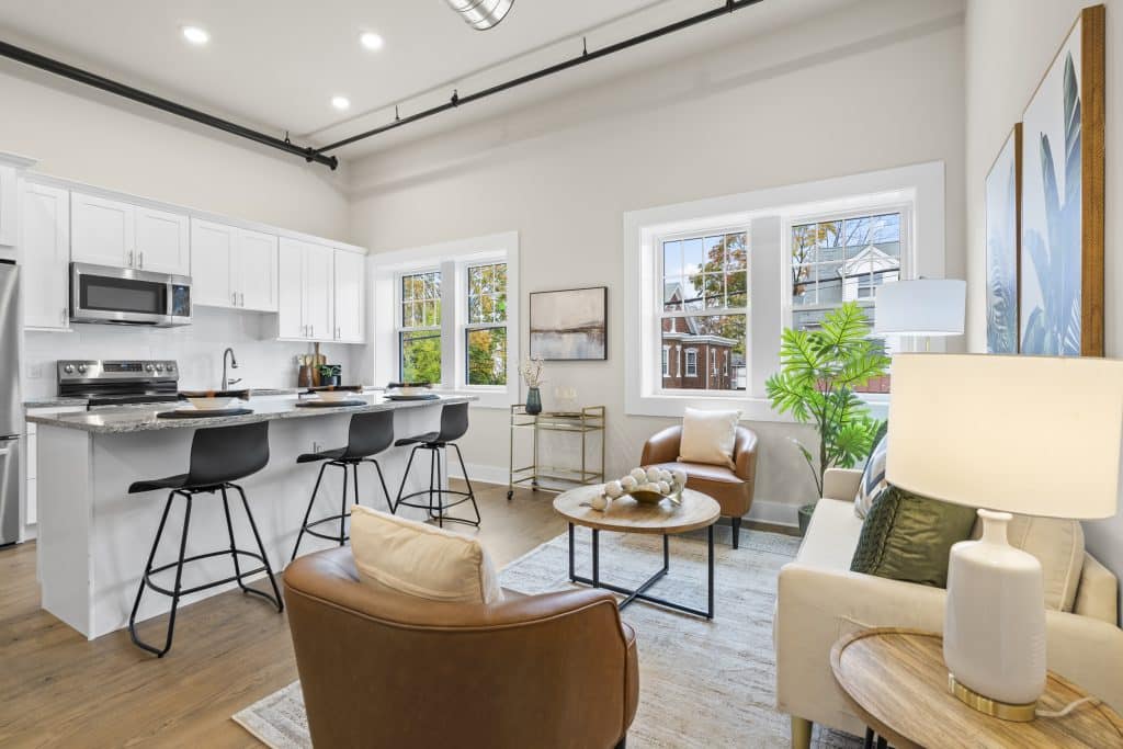 Open-plan loft living room and kitchen at Lofts on Broad with white cabinets, breakfast bar, black stools and leather chairs.