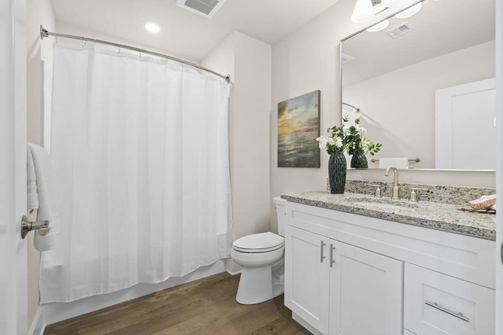 Lofts on Broad bathroom, Souderton PA: white shower curtain, curved rod, vanity with granite top, mirror and floral vase.