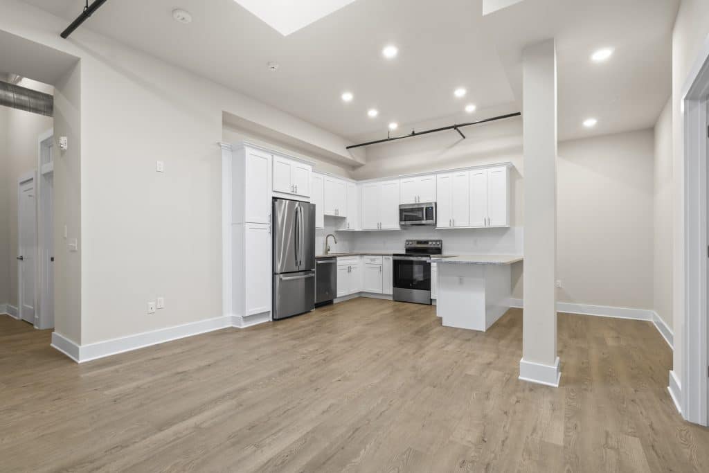 Open kitchen at Lofts on Broad, Souderton PA with white cabinets, stainless appliances, island and wood-look floors.