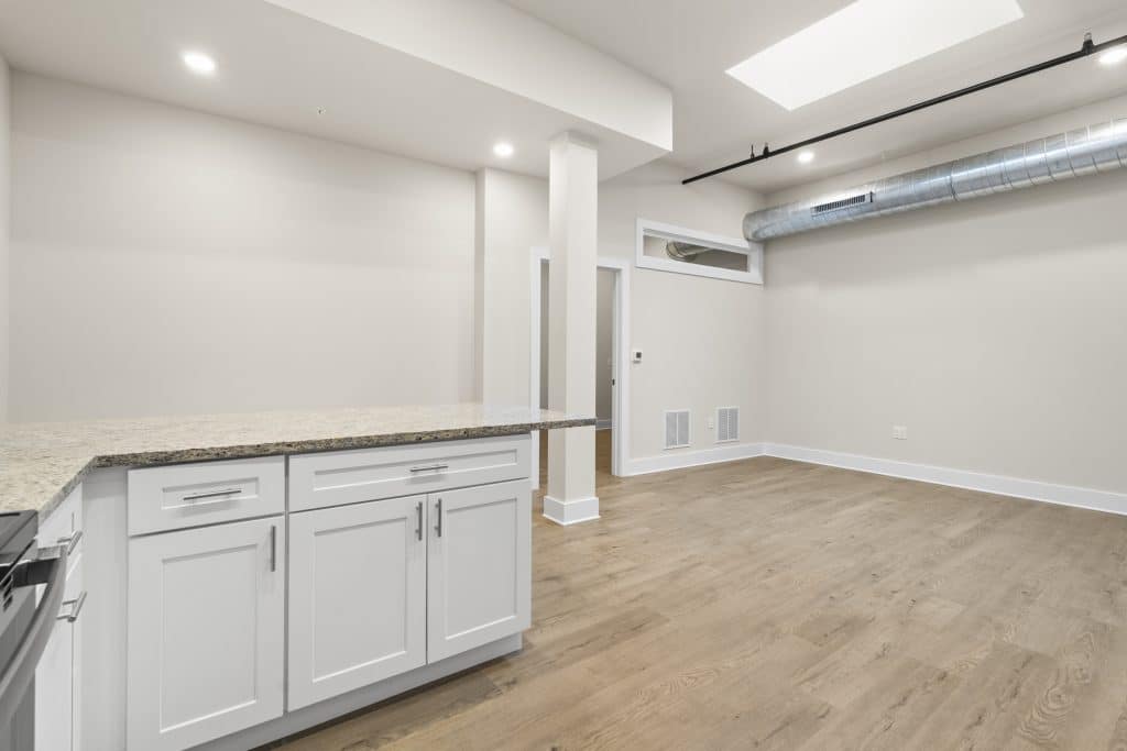 Empty loft at Lofts on Broad, Souderton, with white kitchen cabinets, granite counter, exposed ductwork, and wood floors.