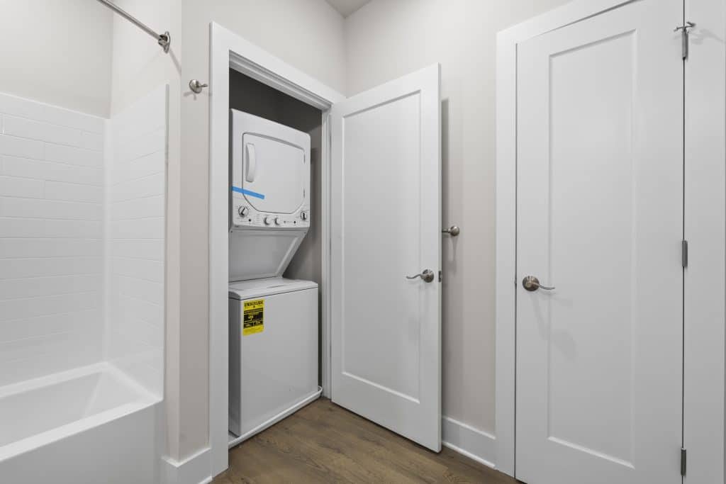 Stacked white washer-dryer in a closet off a bathroom at Lofts on Broad, Souderton, PA, with open white doors and adjacent tub.
