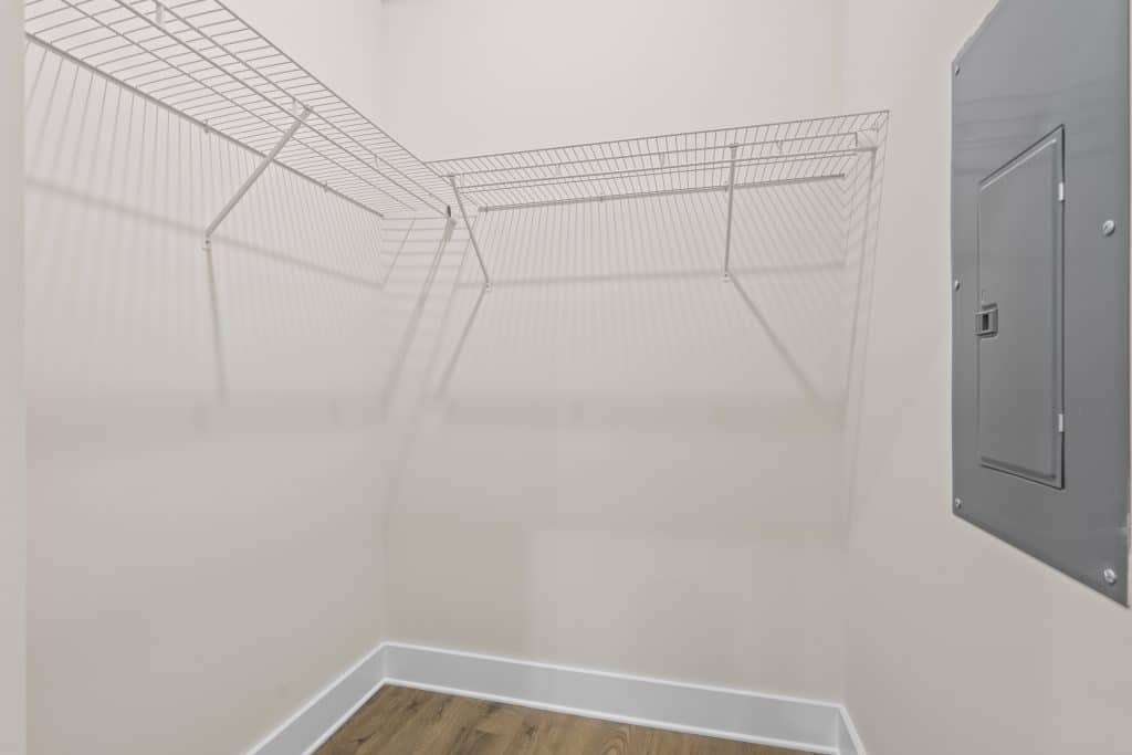 Walk-in closet at Lofts on Broad with white wire shelving on two walls, wood-look floor and a gray electrical panel.