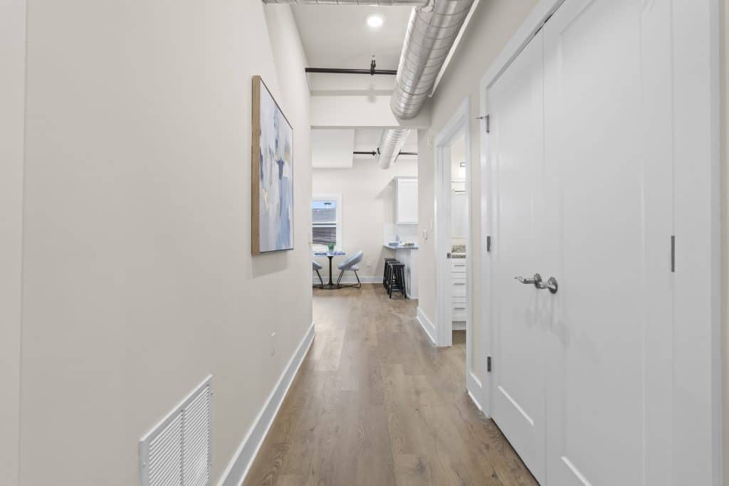 Lofts on Broad hallway with wood floor, white doors, abstract wall art, exposed metal ductwork and view into dining area and kitchen.