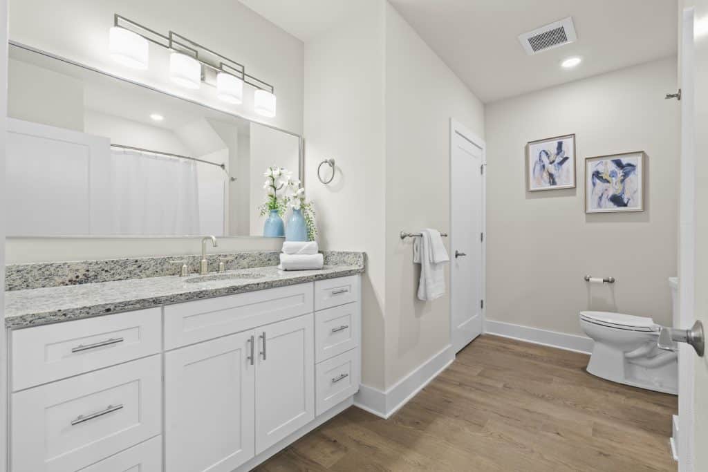 Bathroom at Lofts on Broad with white vanity, granite countertop, mirror, teal vases, toilet and abstract wall art.
