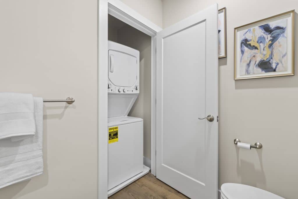 Stacked washer-dryer in a bathroom closet with towel rack and abstract wall art at Lofts on Broad, Souderton PA.