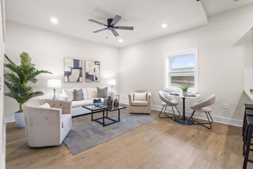 Loft living room at Lofts on Broad, Souderton PA with white sofa, beige chairs, glass coffee table and bistro table by window