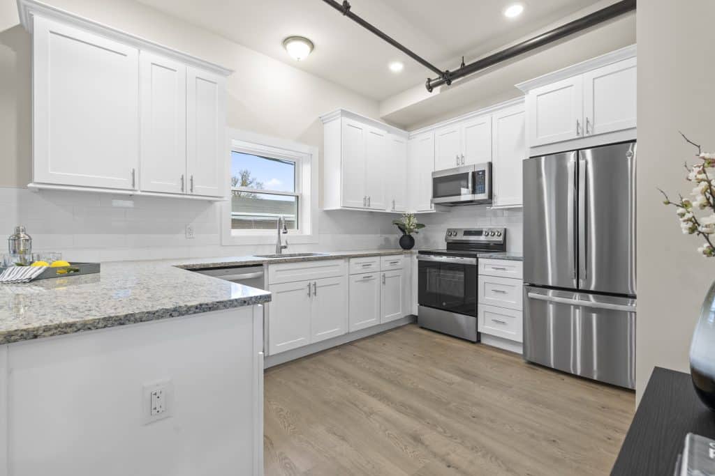 Kitchen at Lofts on Broad, Souderton, PA with white cabinets, granite countertops, stainless fridge and range, and wood floors.