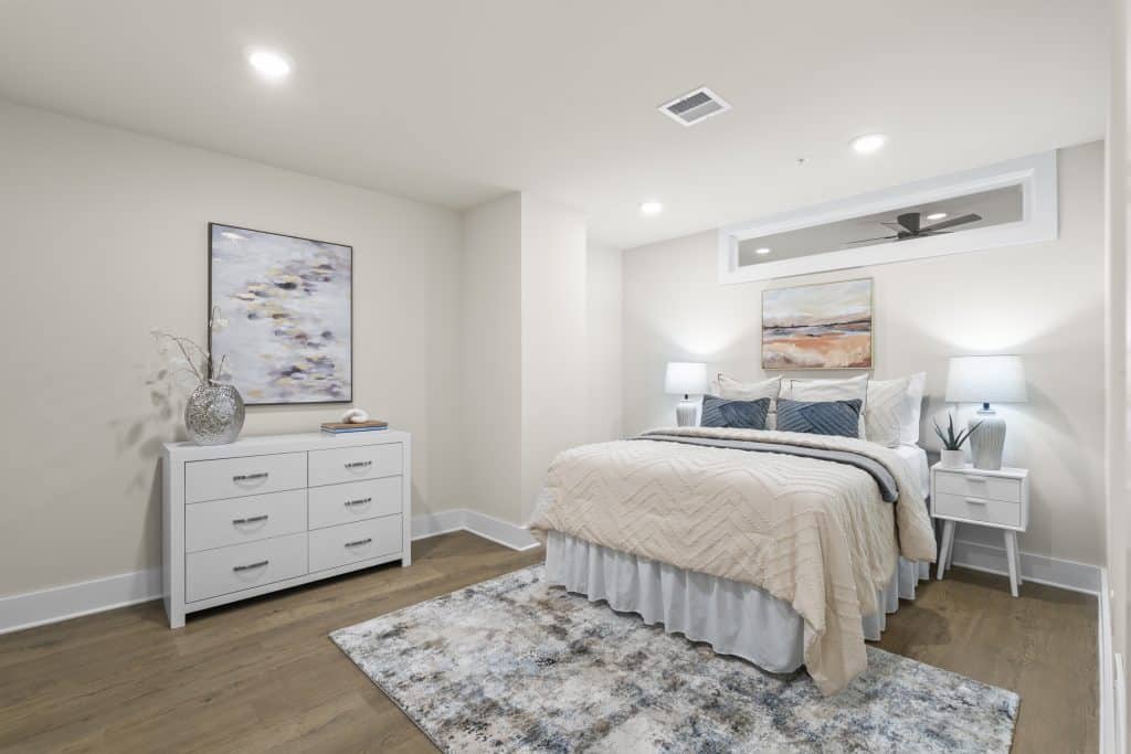 Bright furnished bedroom at Lofts on Broad, Souderton PA, with queen bed, white dresser, nightstands, and abstract art.
