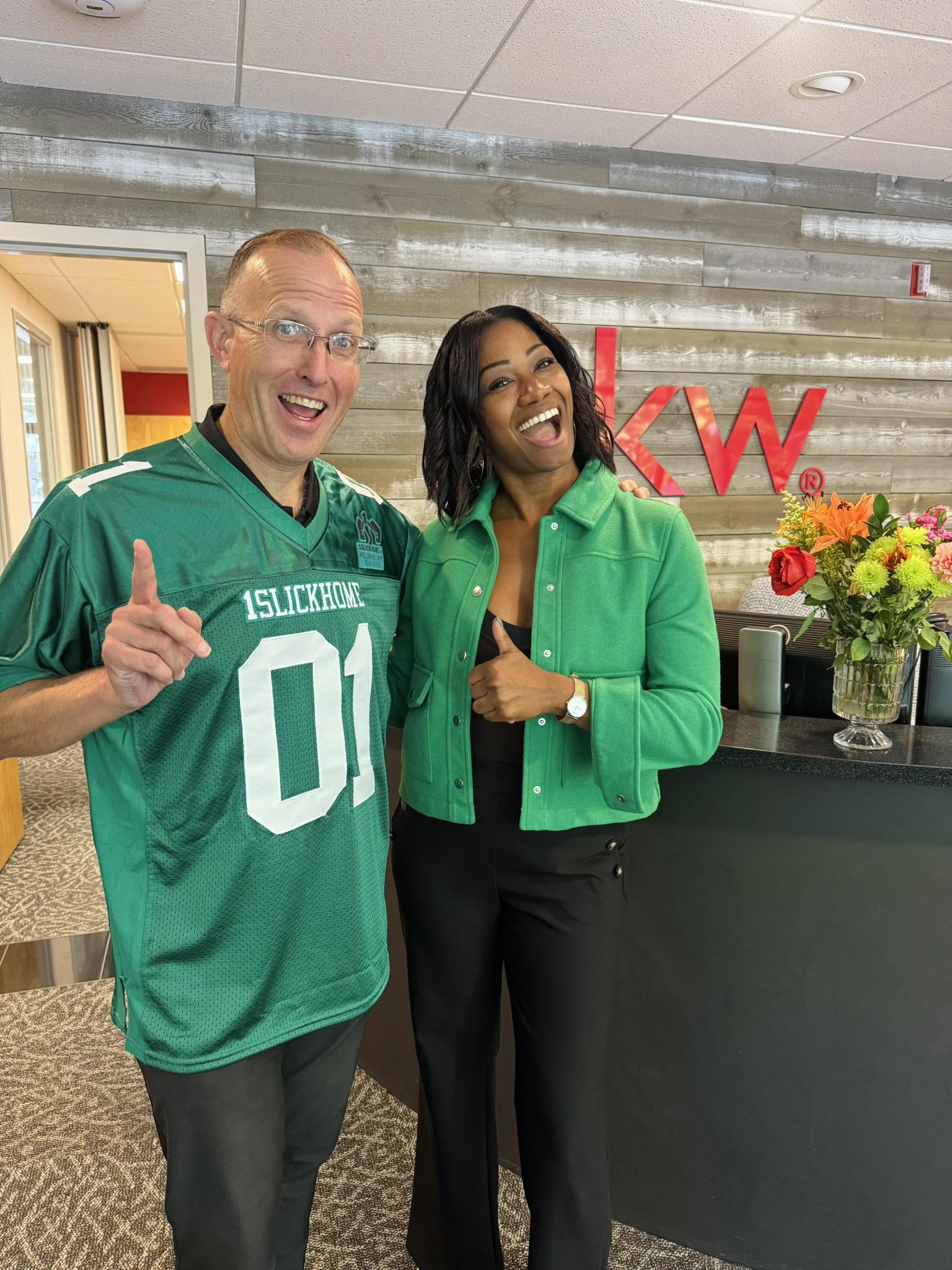 Man in blue jacket and two smiling women pose under a Keller Williams real estate tent at an outdoor community event.