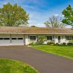 Single-story ranch house with attached two-car garage, light brick exterior, blue shutters, driveway and green lawn.