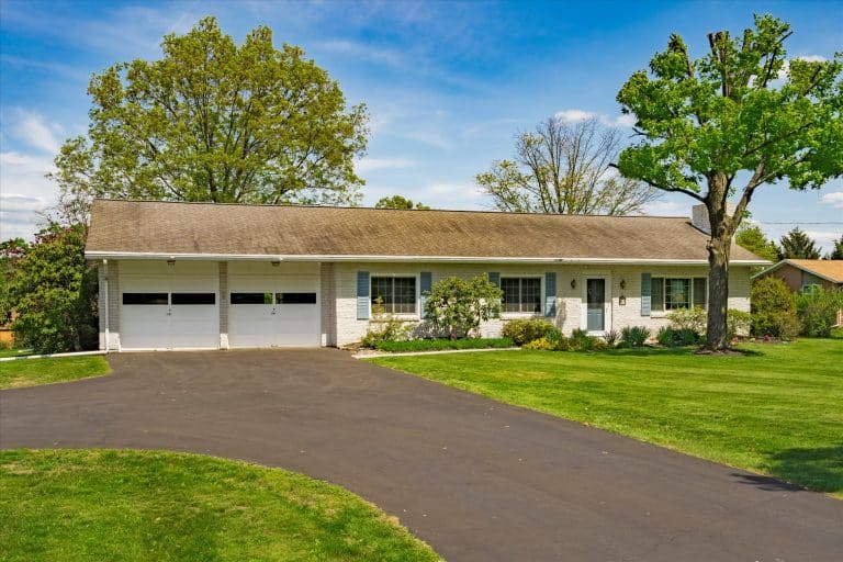 Single-story ranch house with attached two-car garage, light brick exterior, blue shutters, driveway and green lawn.