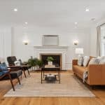 Bright living room with a tan leather sofa, two mid-century chairs, central coffee table, rug, and decorative fireplace