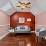 Small sitting room with gray loveseat, accent chair, side table, floor lamp and red feature wall under a ceiling fan.