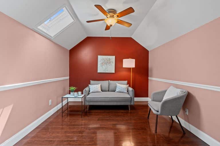 Small sitting room with gray loveseat, accent chair, side table, floor lamp and red feature wall under a ceiling fan.