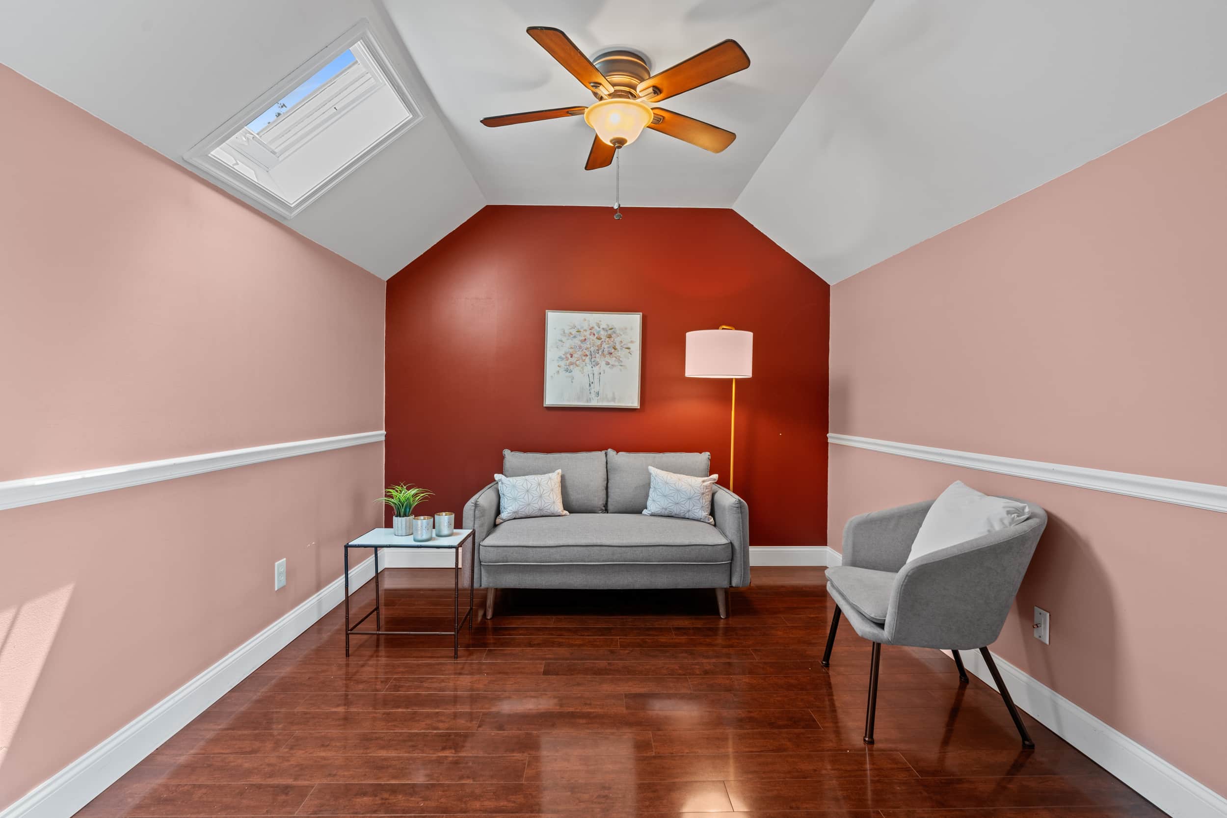 Small sitting room with gray loveseat, accent chair, side table, floor lamp and red feature wall under a ceiling fan.