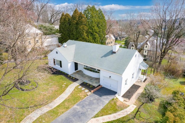Single-story white house with a green roof, attached garage, curved front planter and stone walkway through a grassy yard, viewed from above.