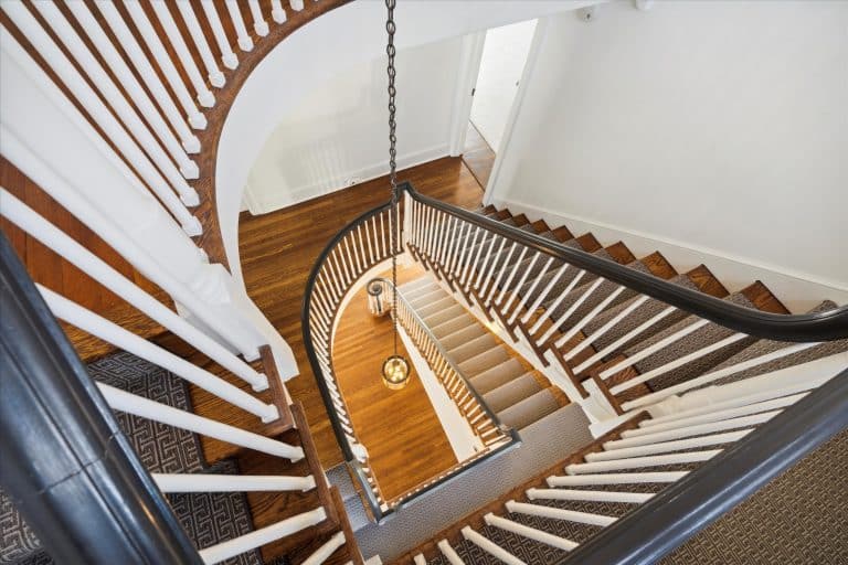 Overhead view of a curved wooden staircase with white balusters, dark handrails, patterned stair runner, and hanging pendant light.